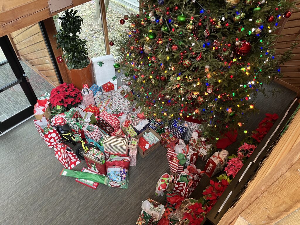 Large Christmas tree in lobby surrounded by wrapped gifts for donation