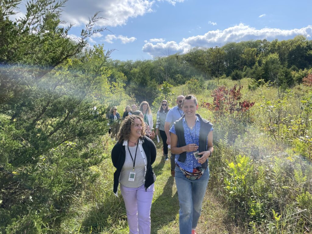 Group of people on a path surrounded by trees, bushes and wildflowers, with blue sky in the background