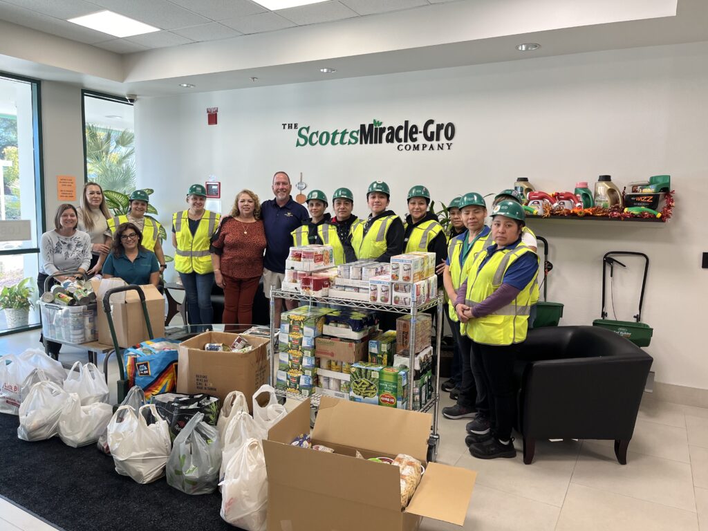 Group of people standing in a lobby surrounded by packages of food to be donated