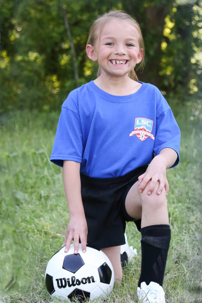 Picture of child kneeling in the grass next to a soccer ball